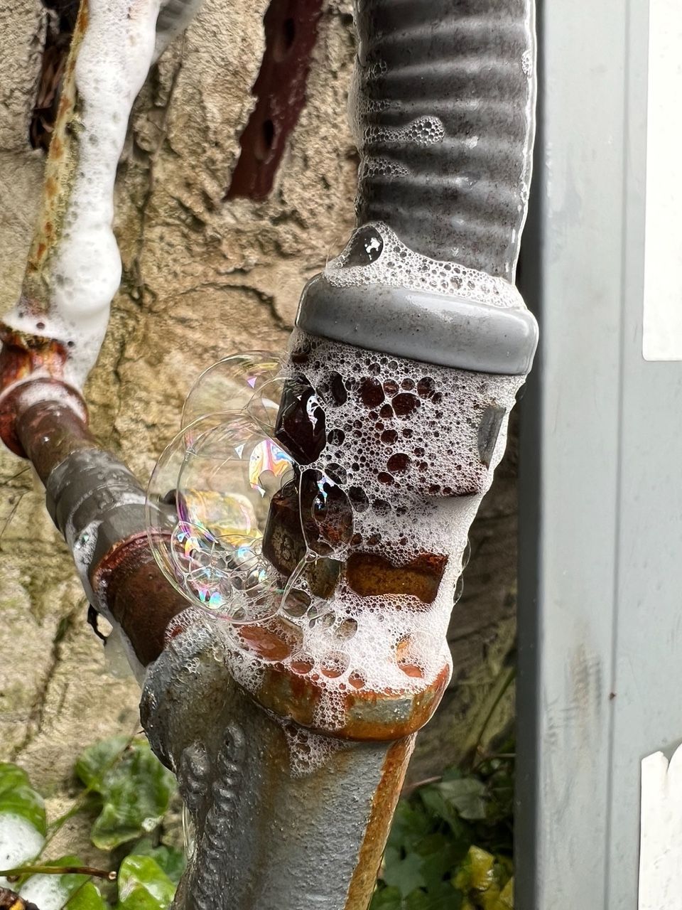 A metal pipe joint leaking gas, indicated by soap bubbles forming on the rusted connection.