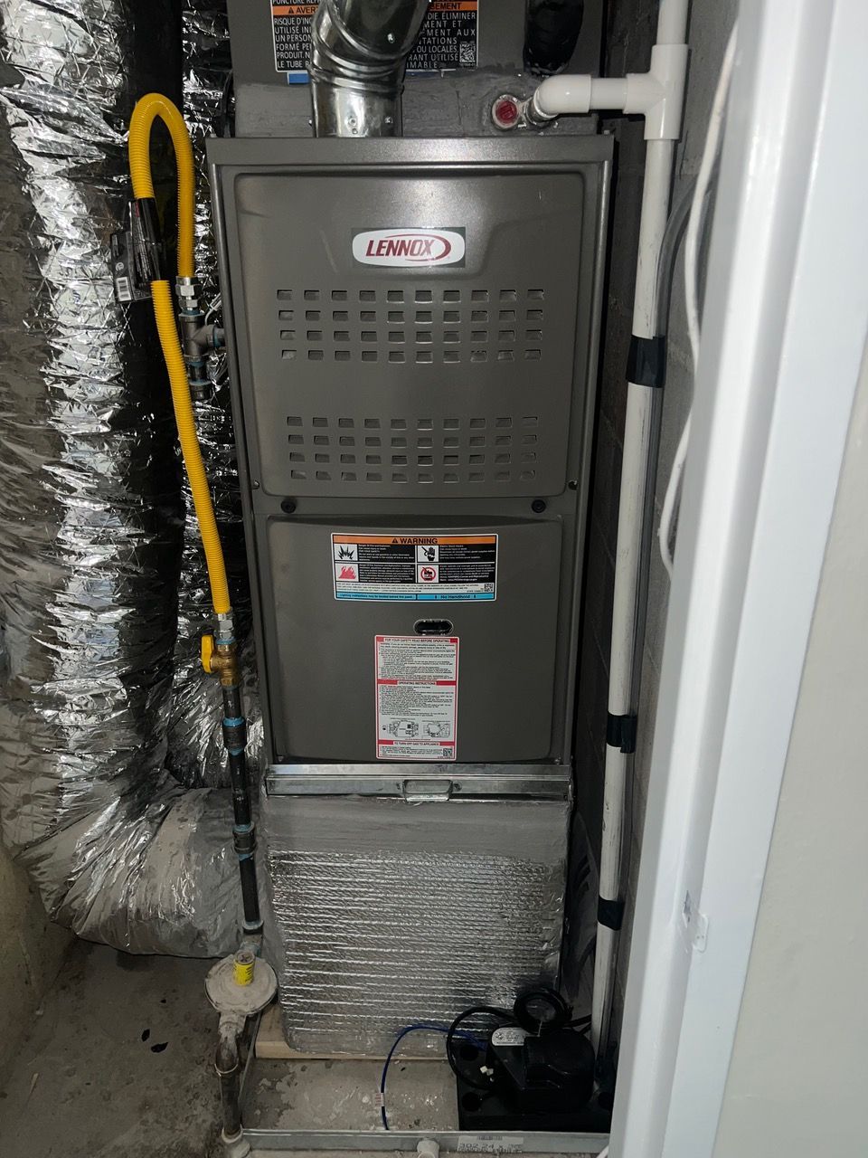 A Lennox furnace unit in a utility closet with a yellow gas line, white PVC piping, and metallic ductwork.