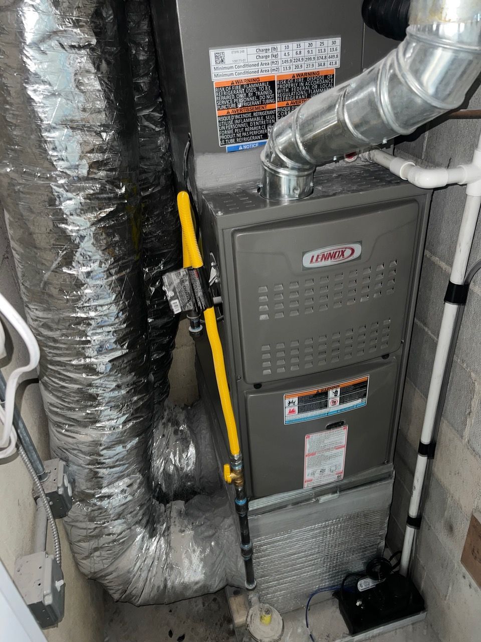 A gray Lennox gas furnace with connected metal ducts and white PVC piping installed in a utility space.