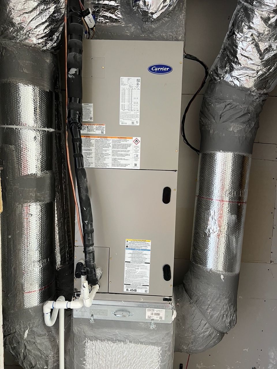 Carrier HVAC air handler unit installed in a utility closet with insulated silver ductwork attached to the sides.