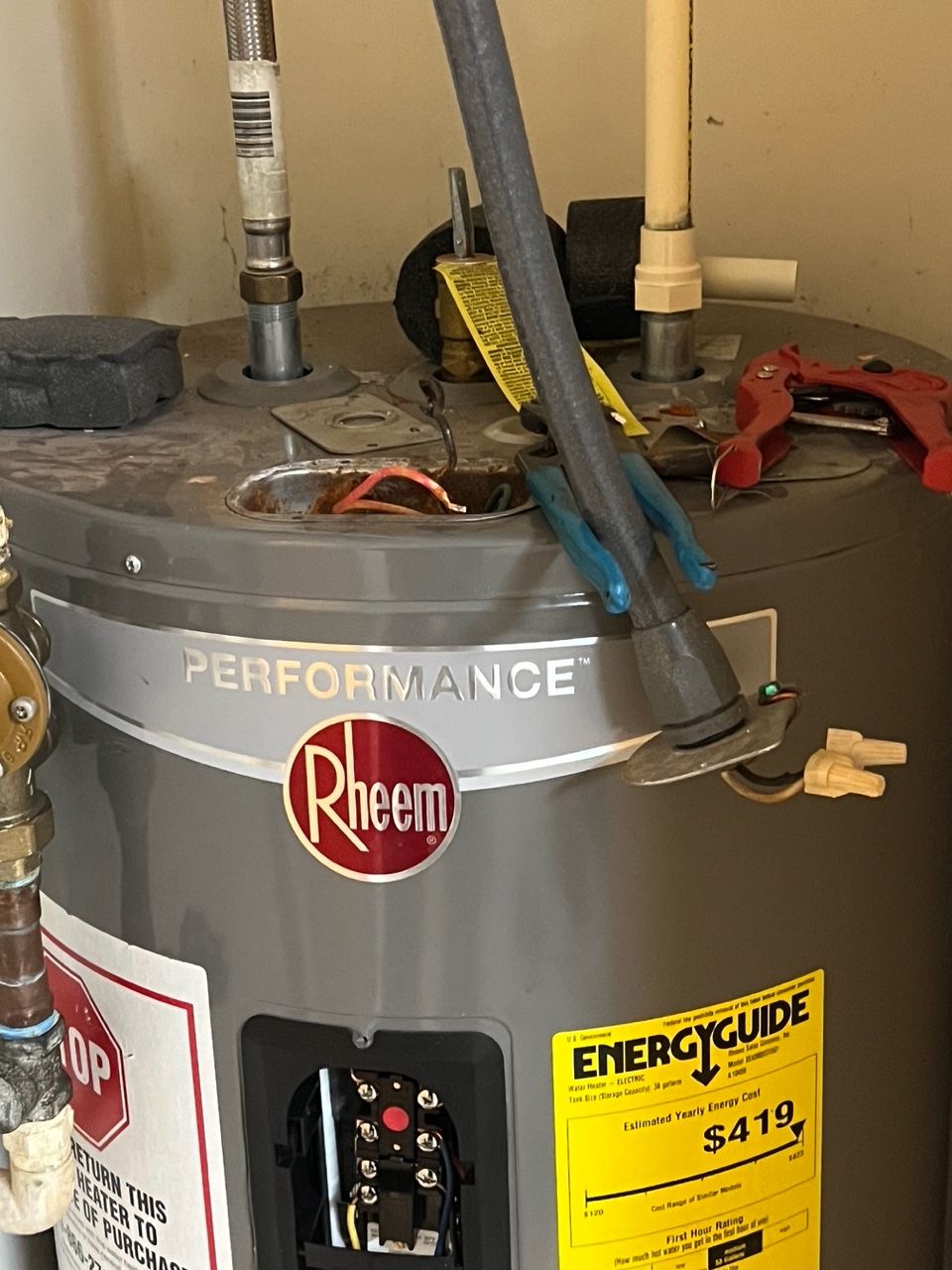 A gray Rheem electric water heater with visible wiring, pipes, and an EnergyGuide label on the front.