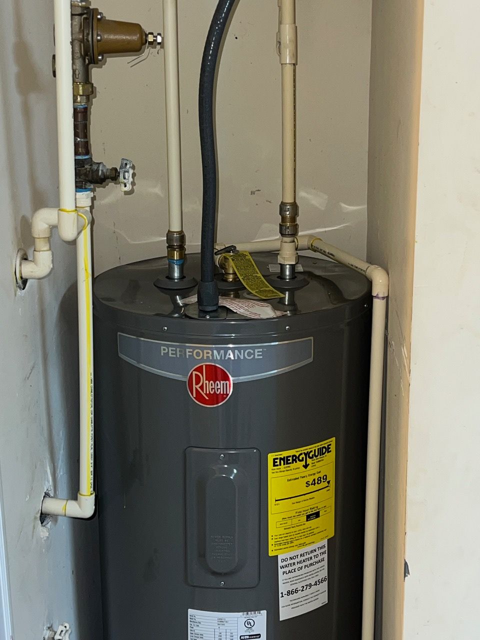 A gray Rheem electric water heater installed in a closet with exposed plumbing connections and a yellow energy label.