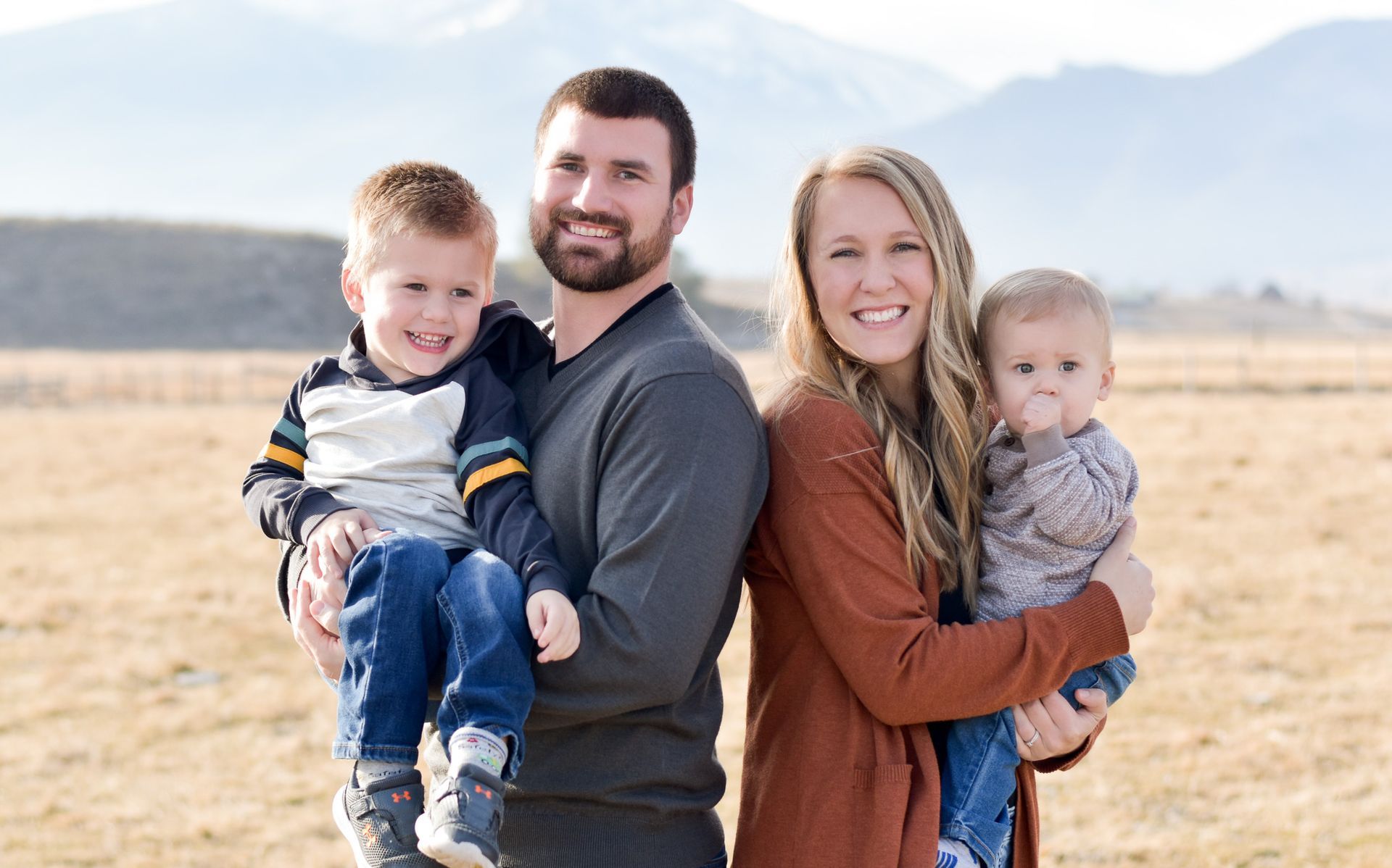 a family is posing for a picture in a field with mountains in the background .