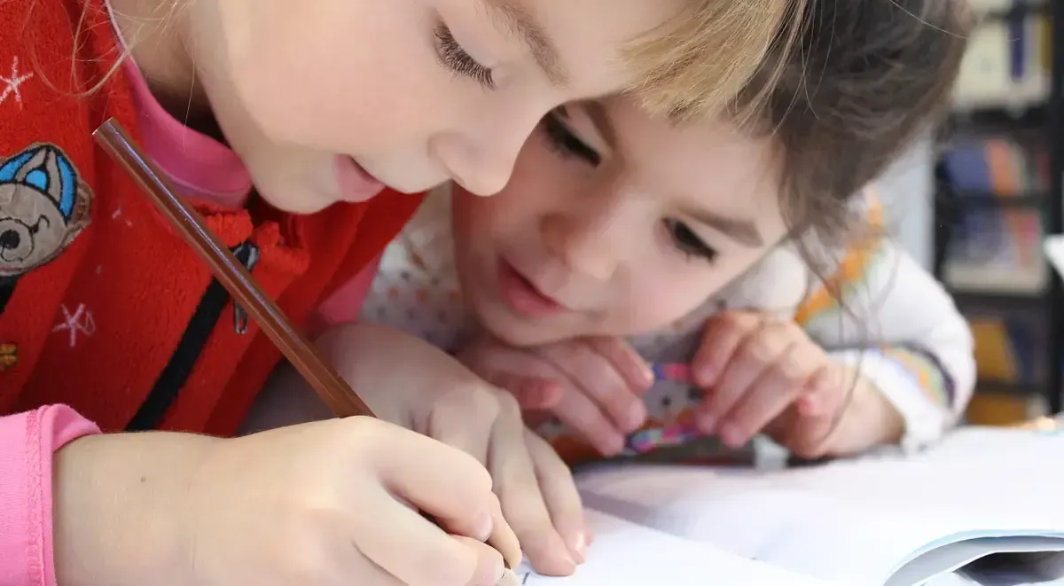 two young girls are sitting at a table writing in a notebook .