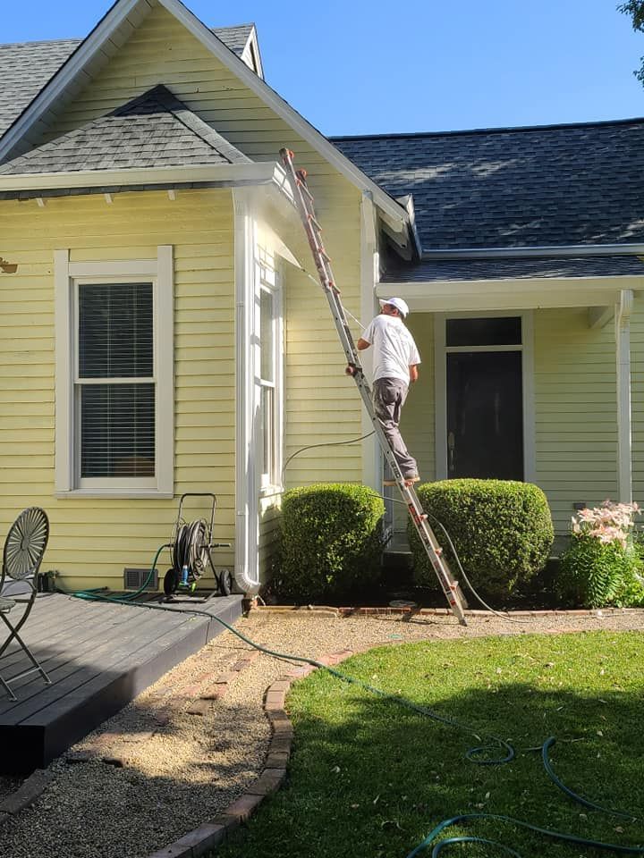 Worker painting a yellow house exterior from a ladder beside the front porch