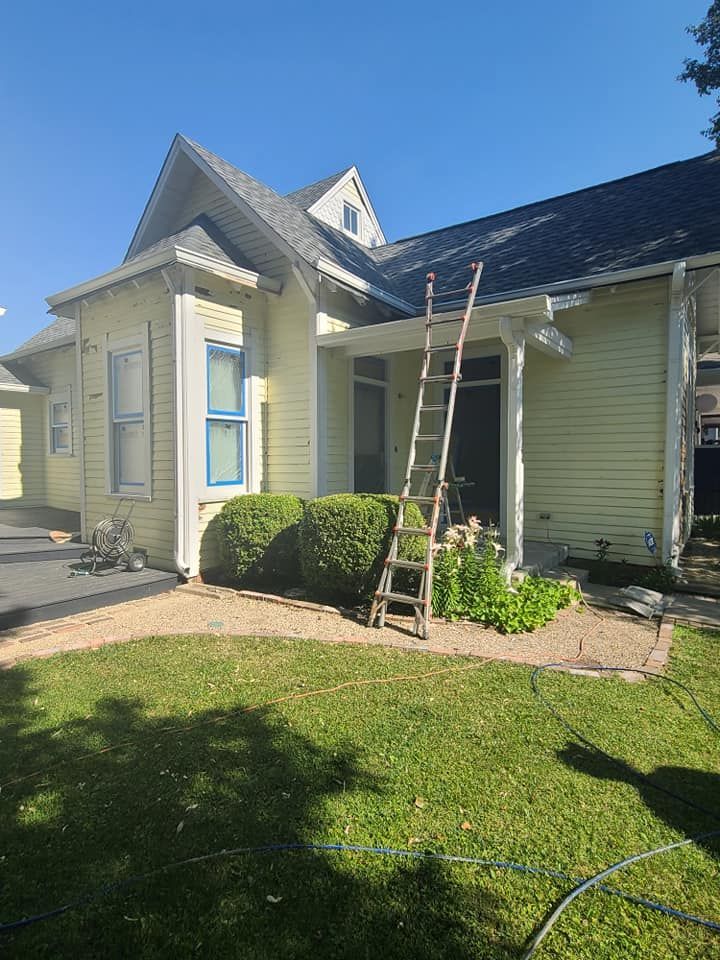 Victorian-style house exterior with a ladder leaning by the front porch and trimmed bushes in the yard