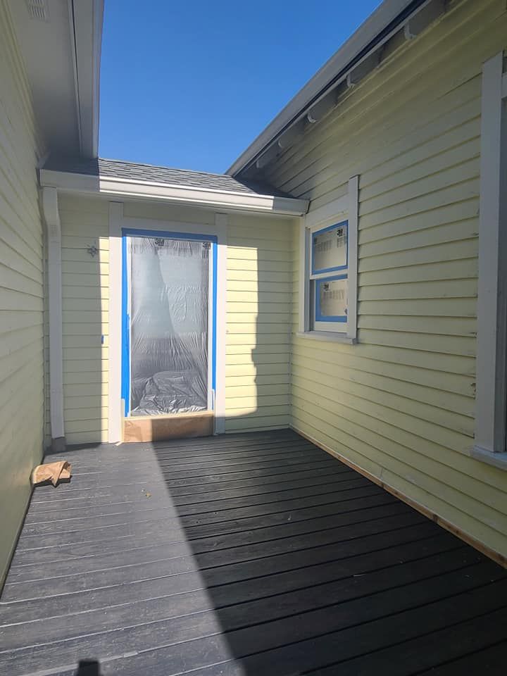 Covered outdoor walkway with yellow siding, dark decking, and a door at the end.