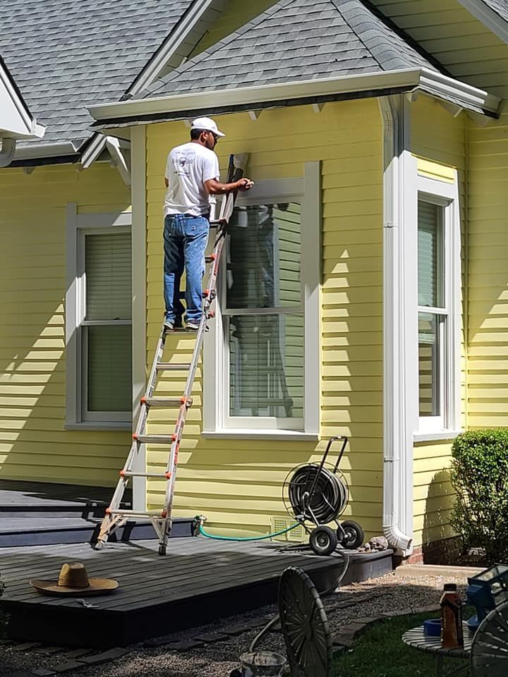 Worker on a ladder painting a yellow house exterior near a window
