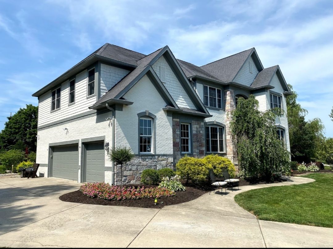 Two-story gray suburban house with double garage, landscaped yard, and blue sky