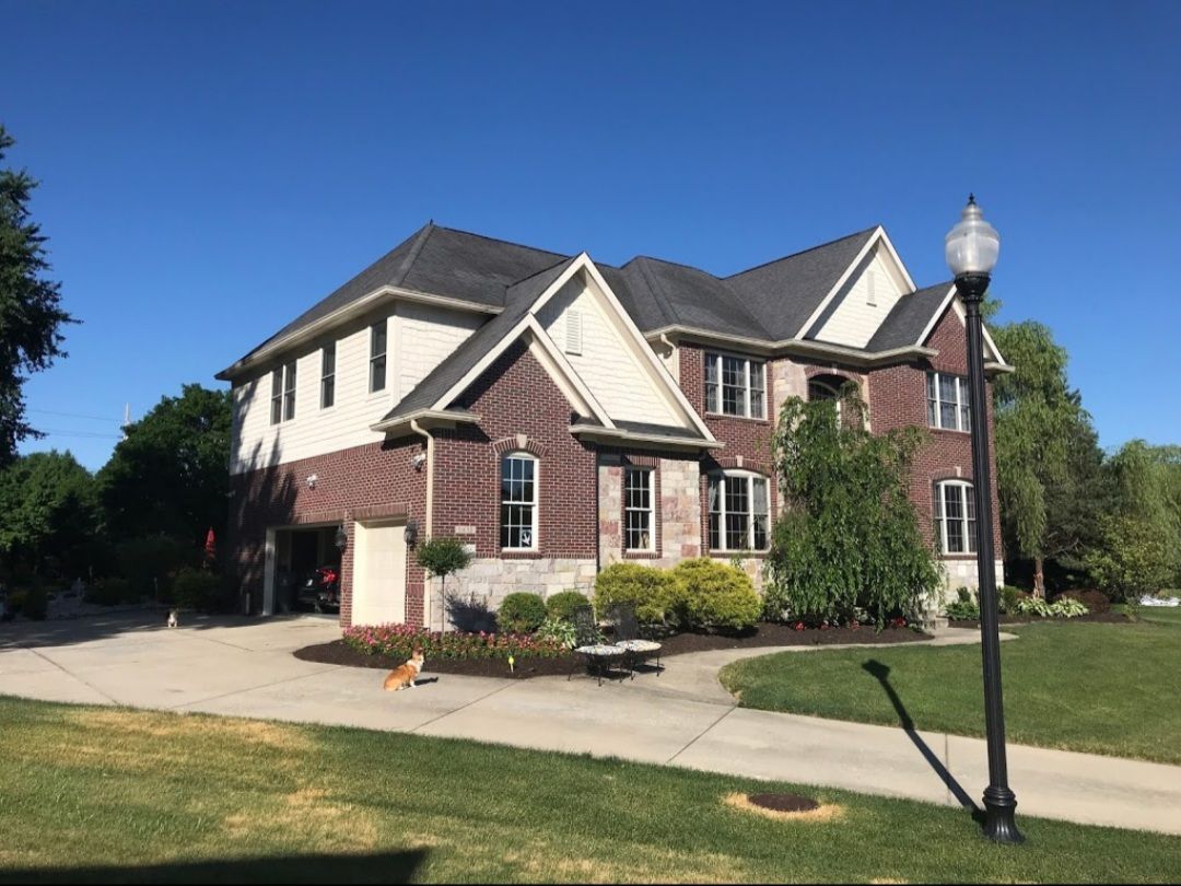 Suburban brick-and-siding house with manicured lawn, driveway, and a lamppost under a blue sky