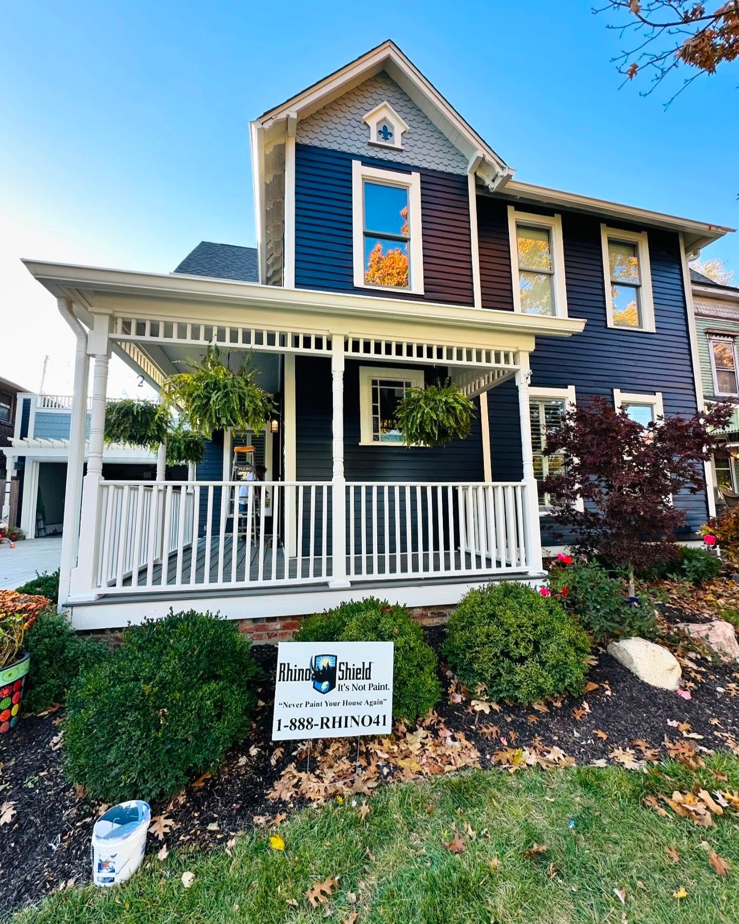 Front porch of a blue two-story house with white railings and a real estate sign in front.