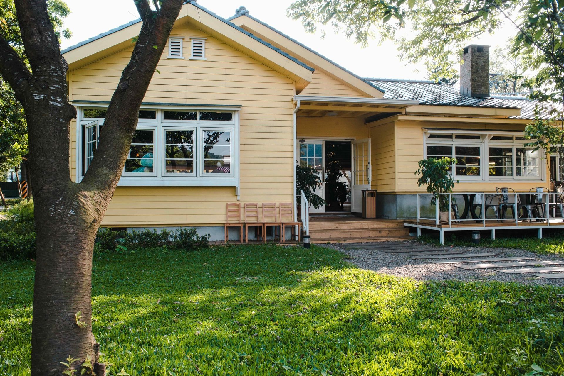 Yellow house with front porch, windows, and a green lawn shaded by trees