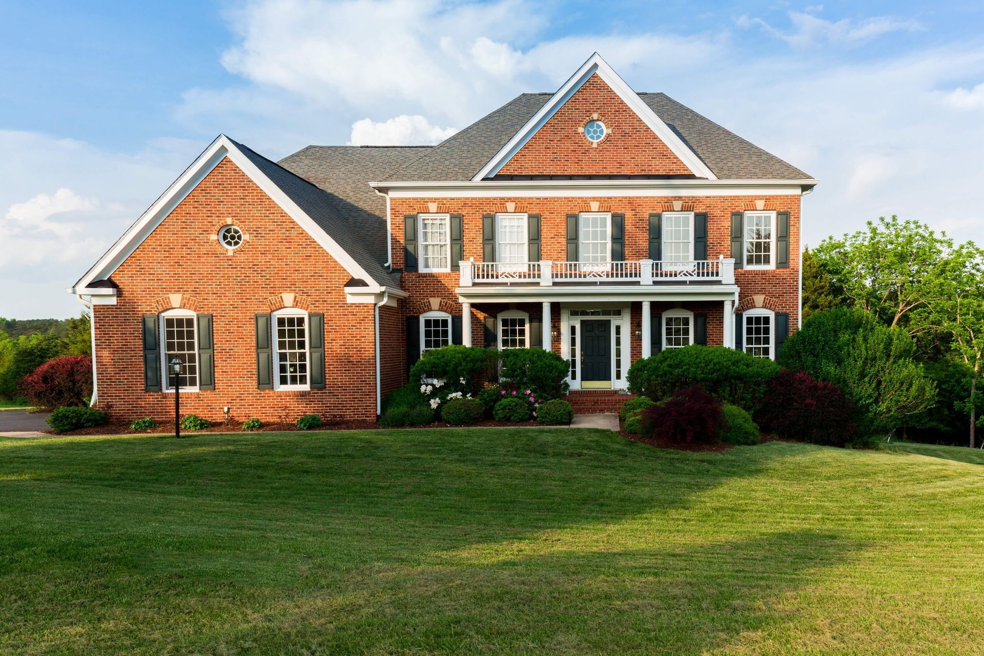 Large red-brick suburban house with white trim and a wide green lawn