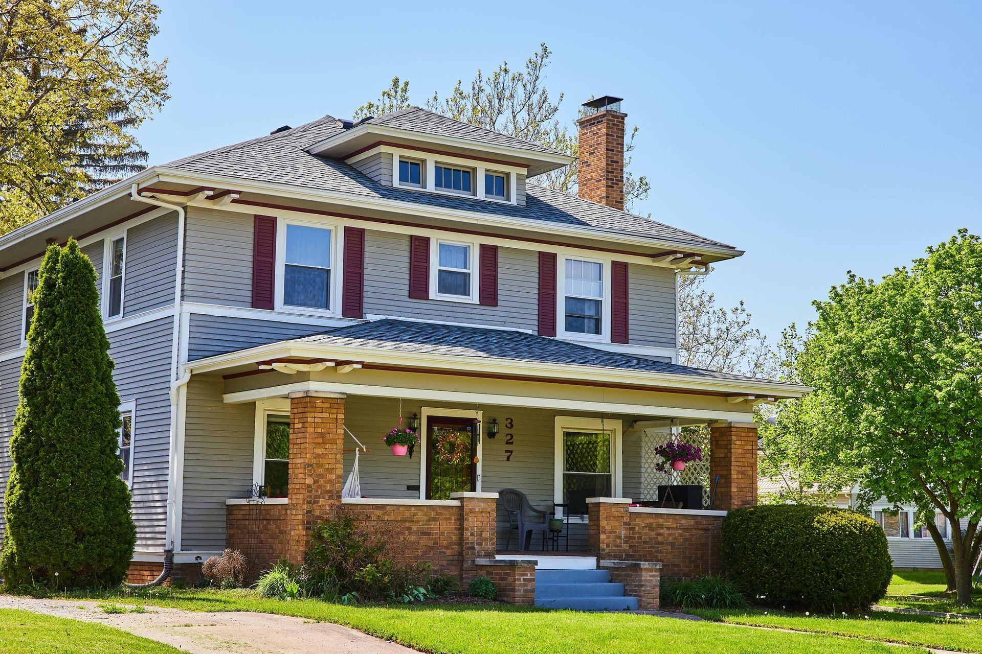 Two-story suburban house with red shutters, white siding, and a front porch on a sunny day
