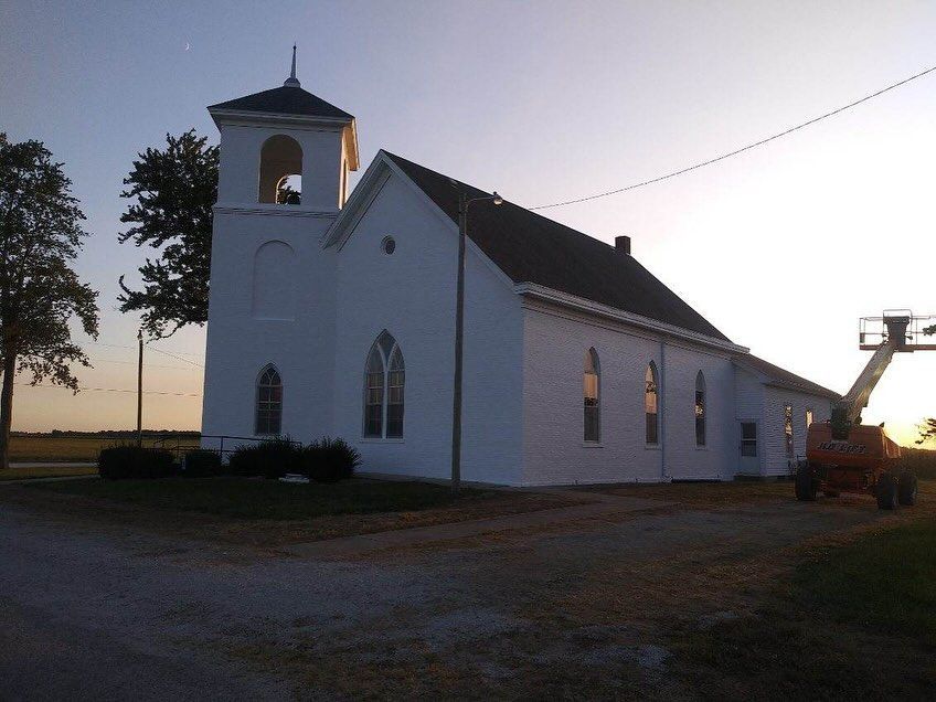 White church at dusk with a bell tower and a backhoe beside it