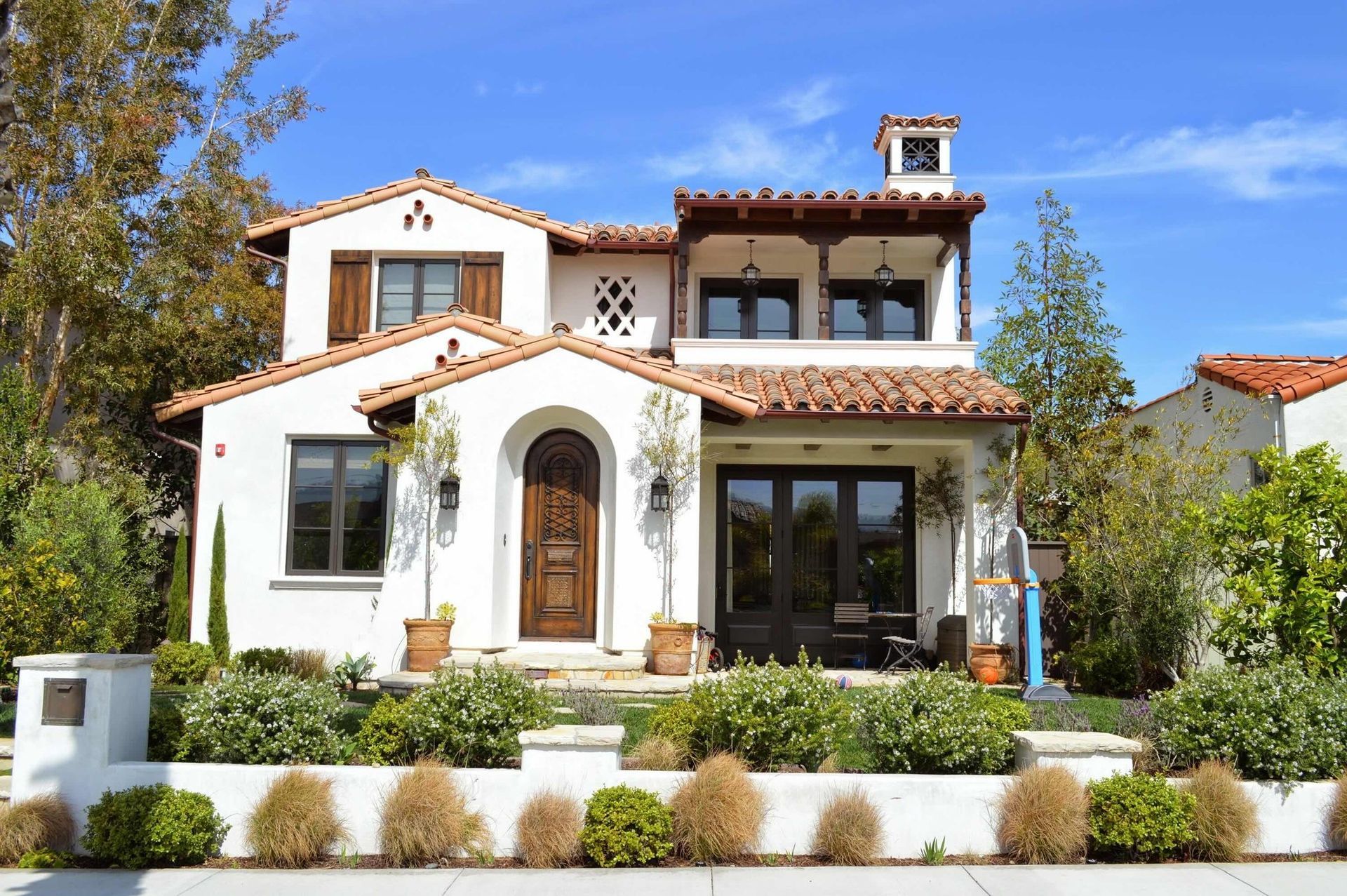 Spanish-style two-story house with white stucco, terracotta roof, and a landscaped front yard