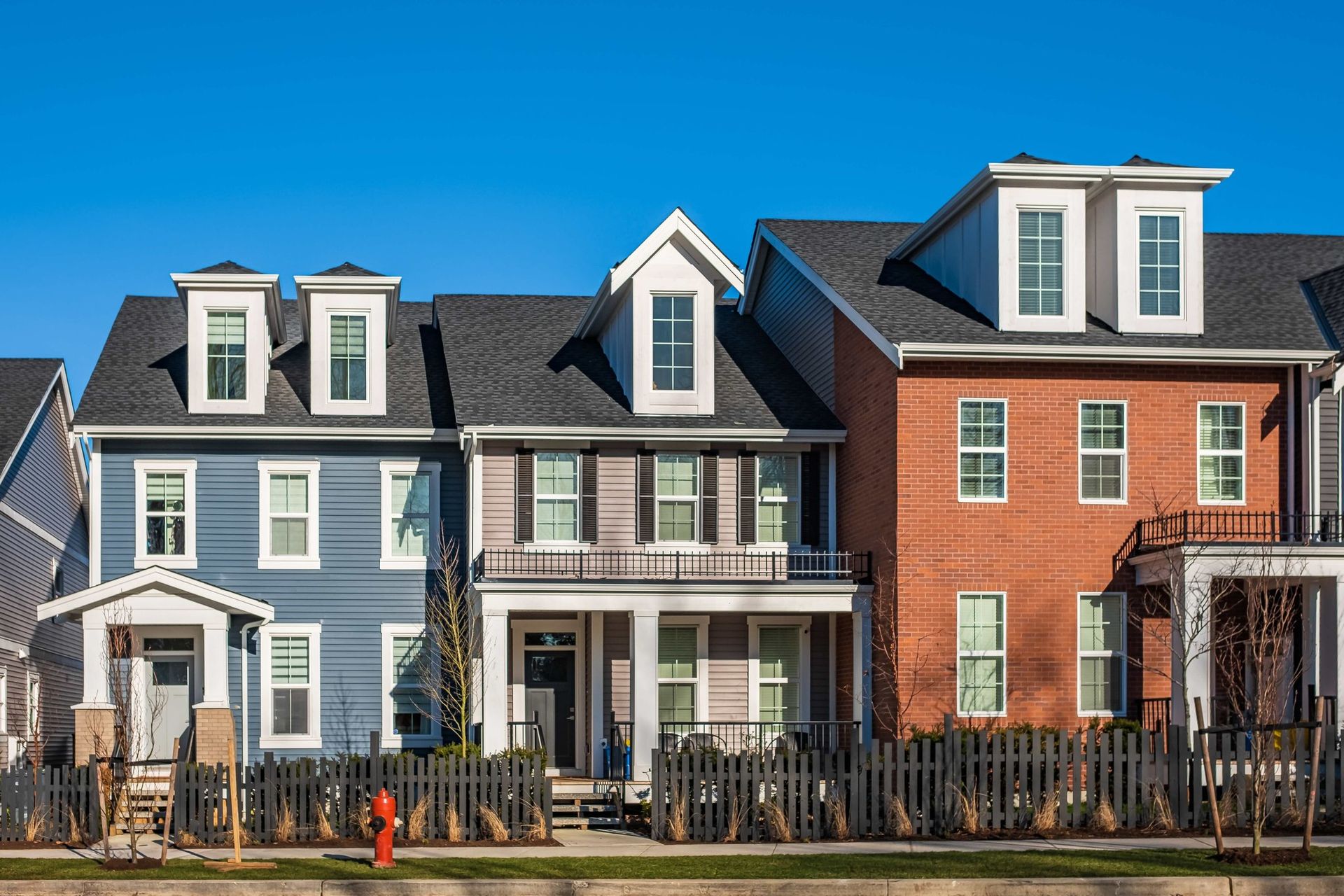 Row of colorful townhouses with front porches and dormer windows on a sunny street