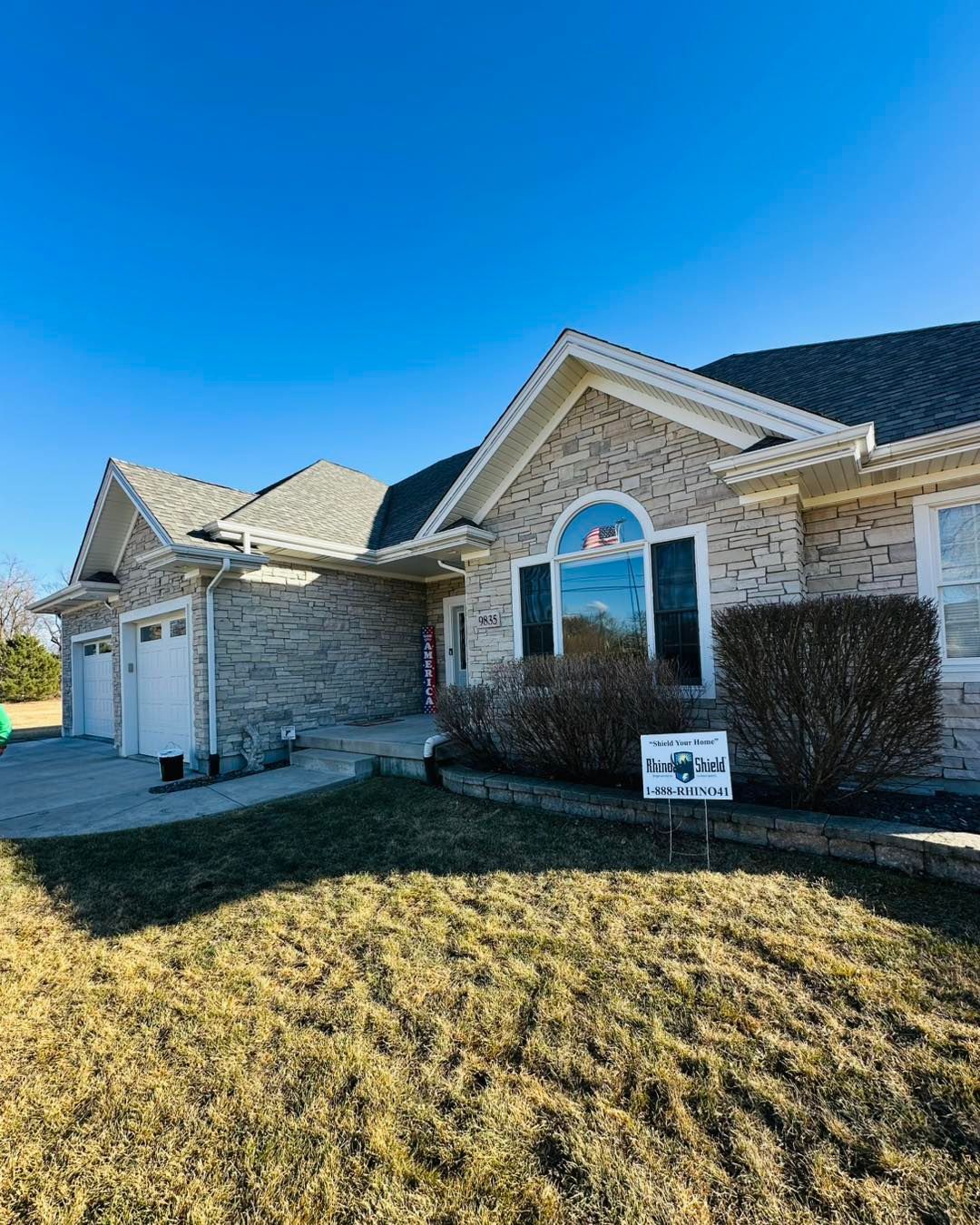 Suburban brick house exterior with blue sky, arched window, and a small front lawn sign