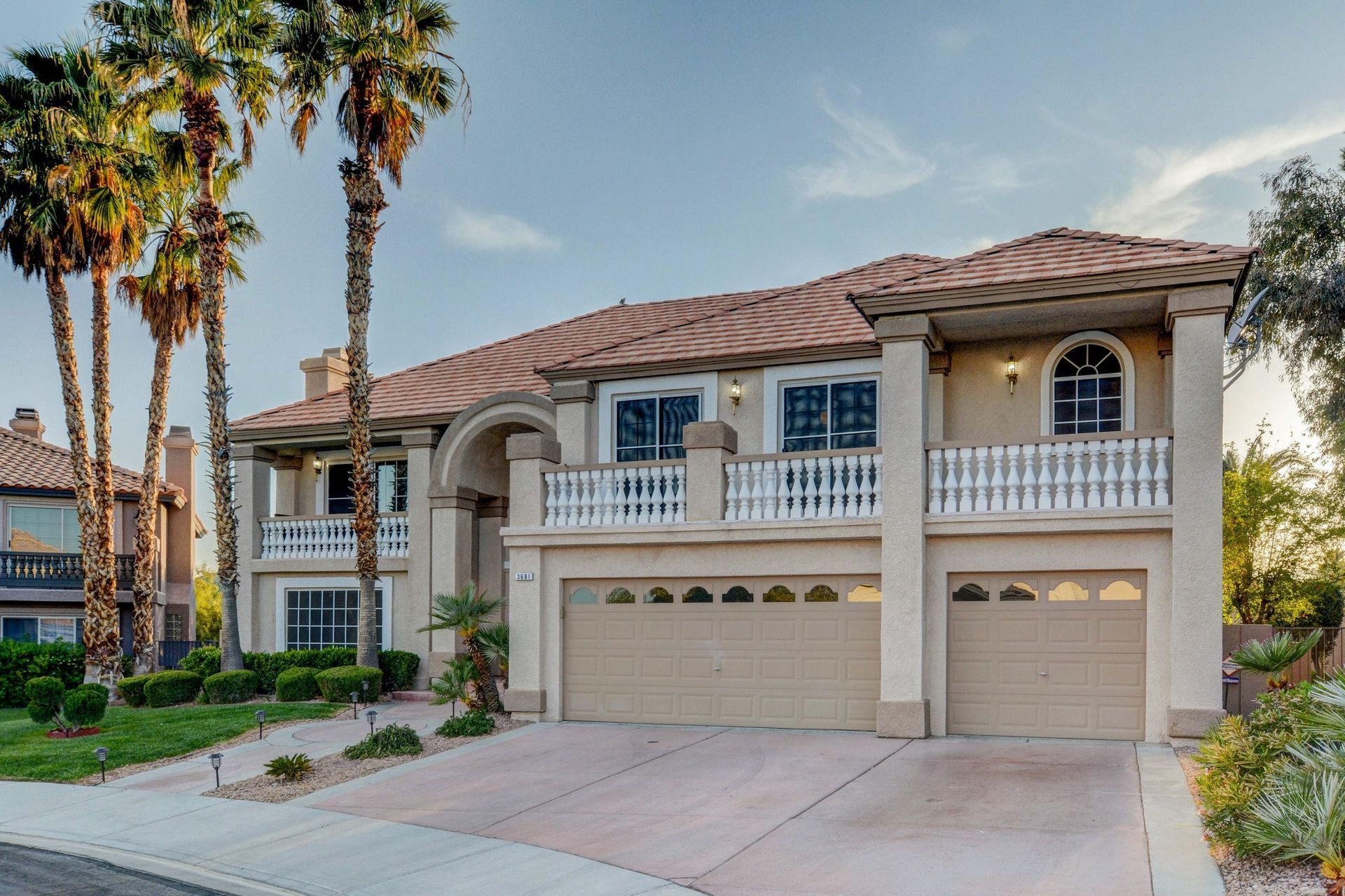 Two-story beige suburban house with a double garage and palm trees along the driveway