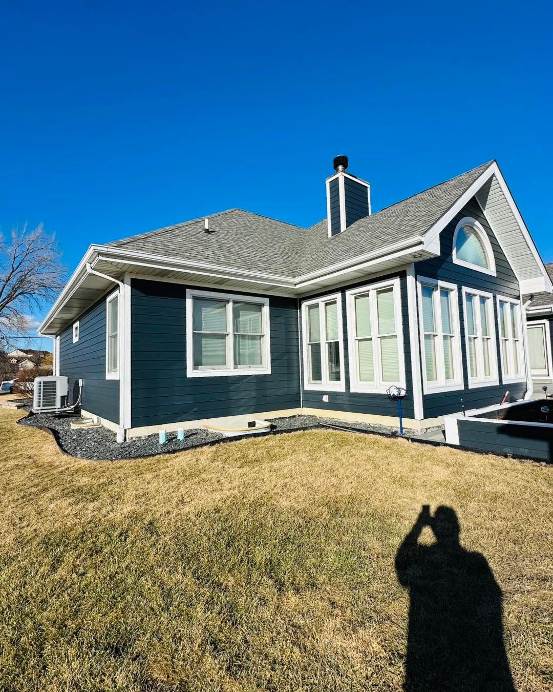 Blue single-story house with white trim and a gabled roof on a sunny day, viewed from the front lawn.