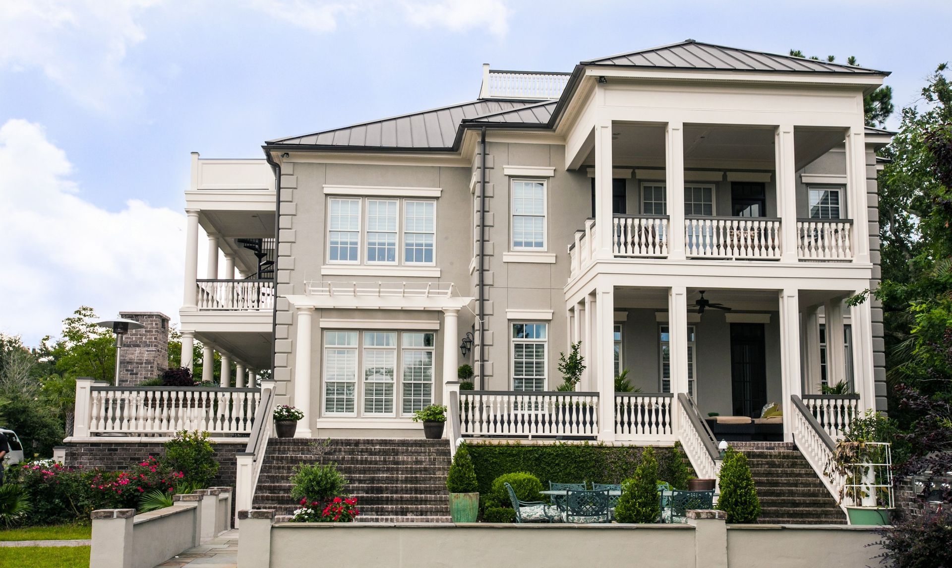 Large white two-story modern house with columns, balconies, and a landscaped front yard