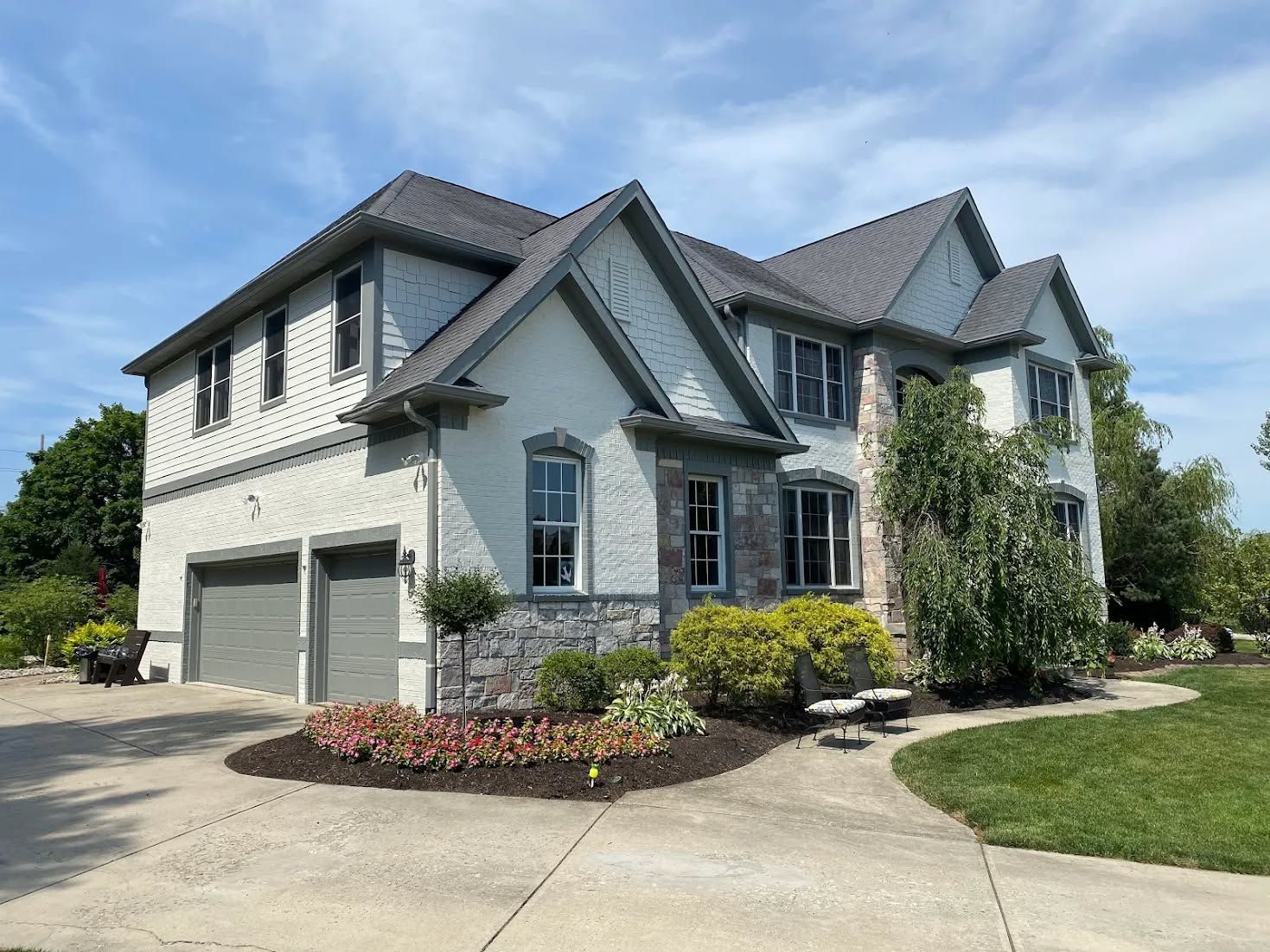 Large white two-story suburban house with gray roof, garage, landscaped yard, and curved driveway