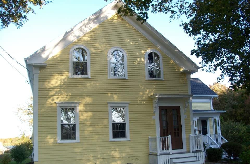 Yellow two-story house with white trim, arched windows, and a small front porch under trees