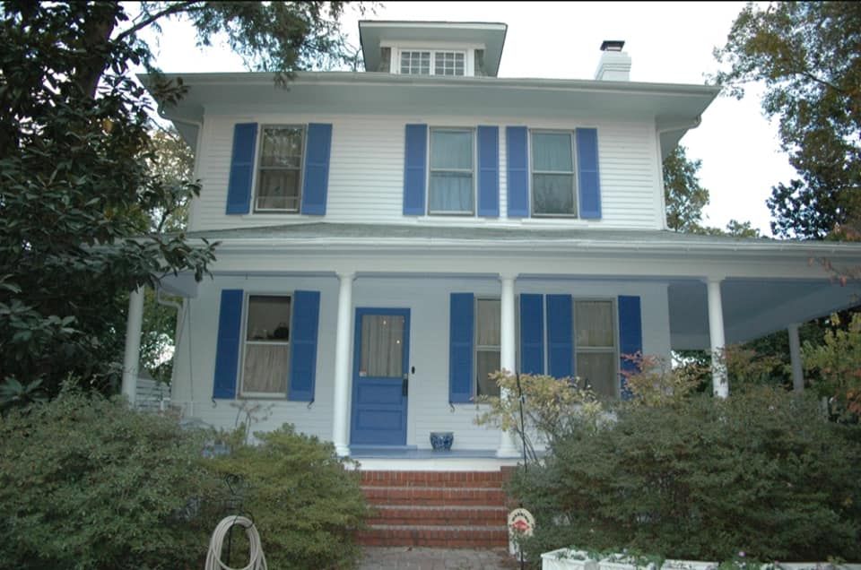 Blue-and-white house with a front porch, brick steps, and shrubs in the yard