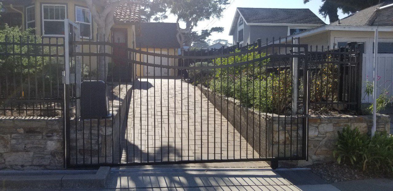 Gated driveway leading to a house with a sunlit path and garden on both sides