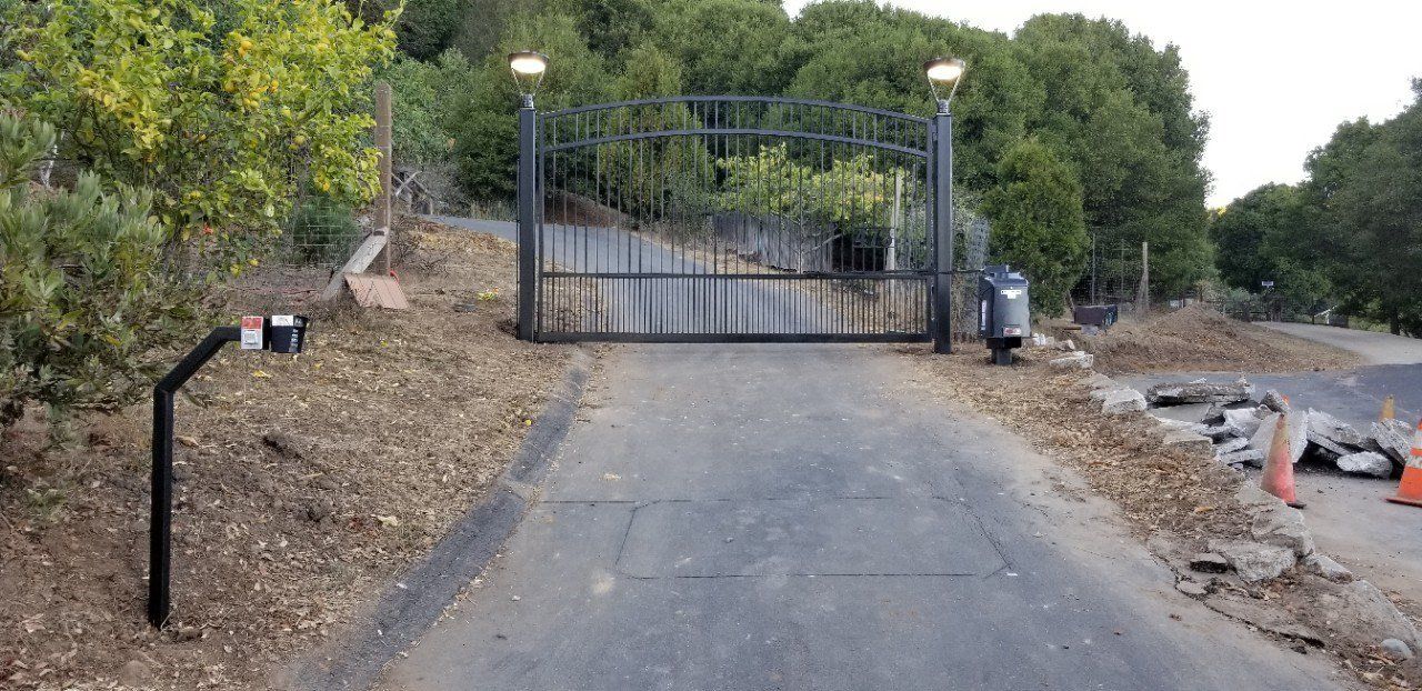 Blocked driveway with a closed metal gate, flanked by dirt embankments and trees.