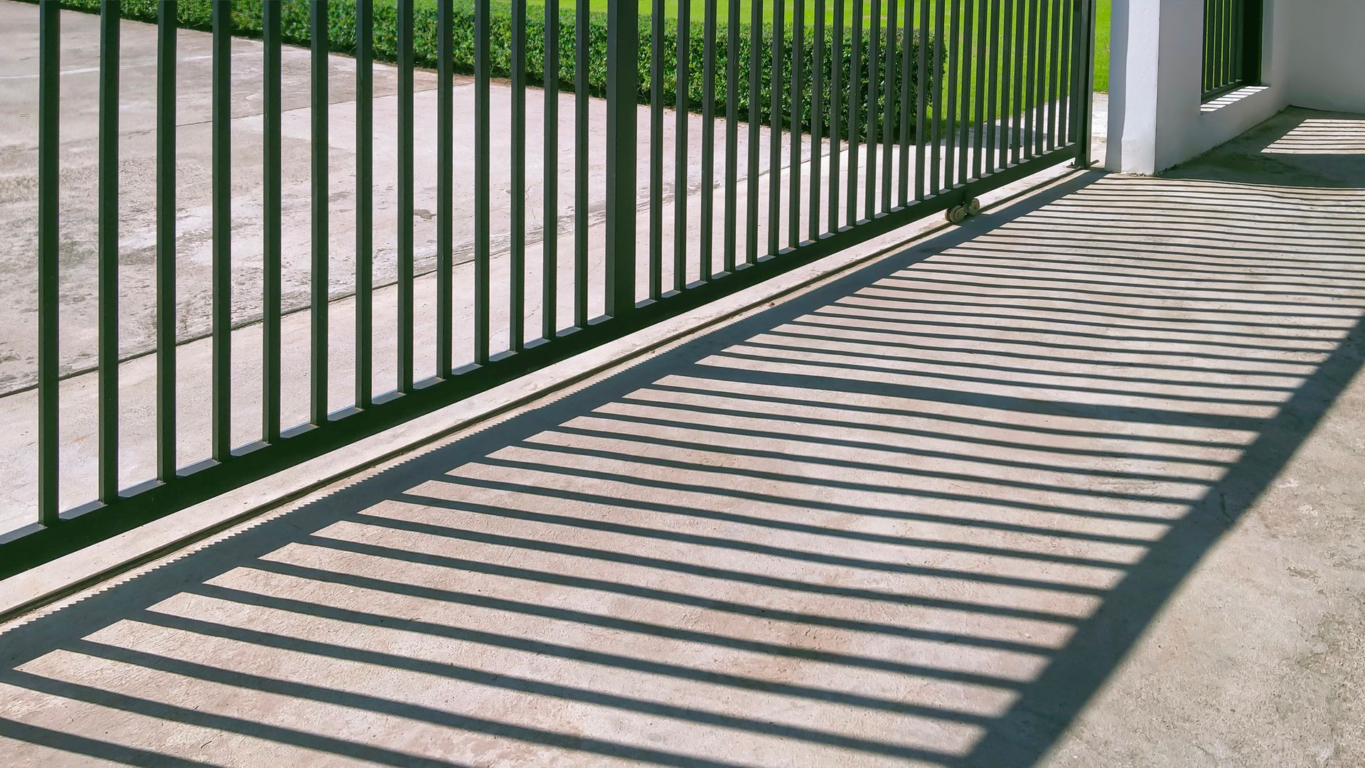 Black metal sliding gate casting long shadows across a concrete driveway.