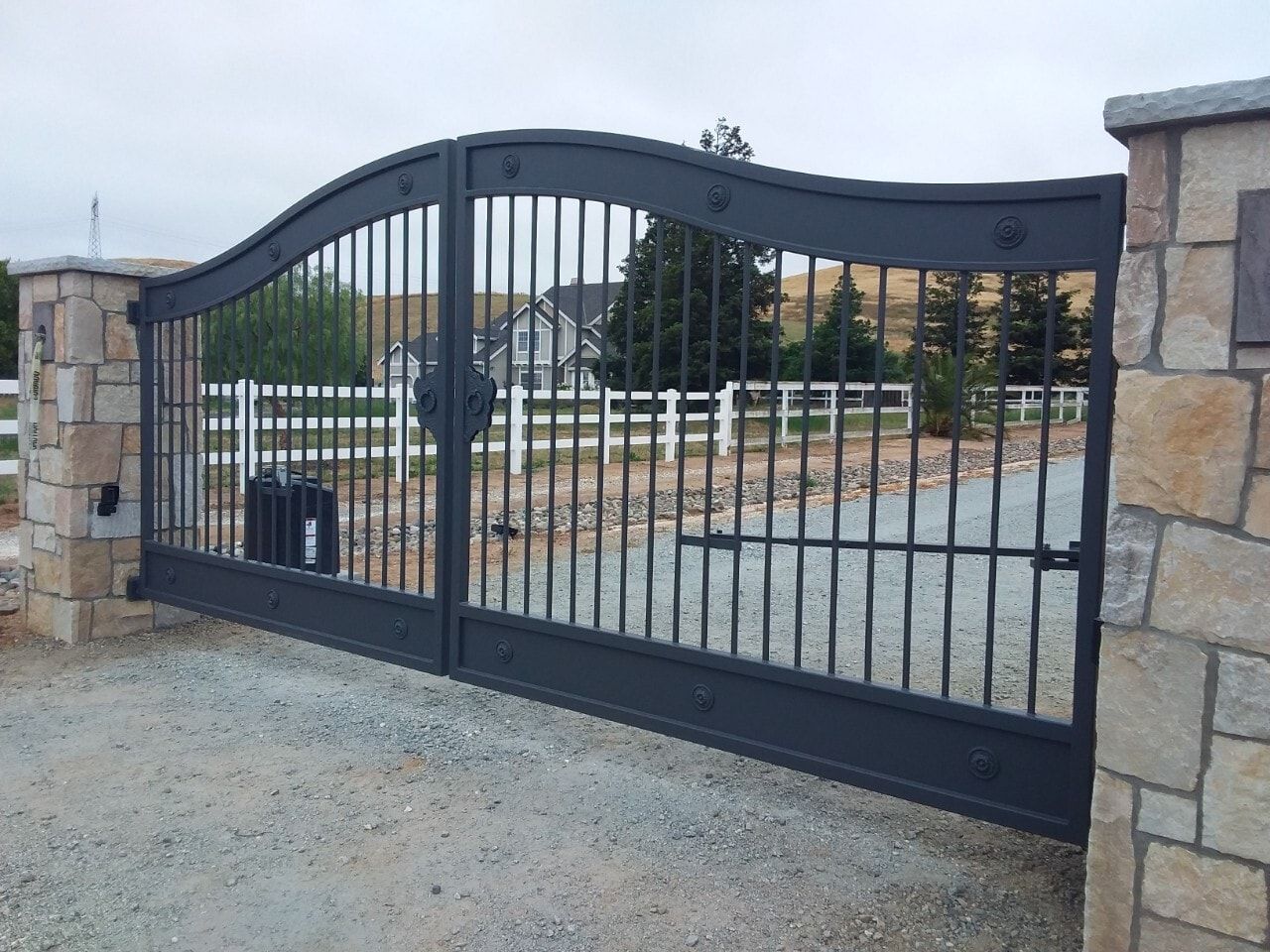Black metal driveway gate with stone pillars at a residential entrance