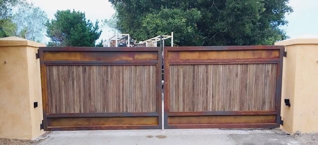 Wooden driveway gate with tan stucco pillars and trees behind it