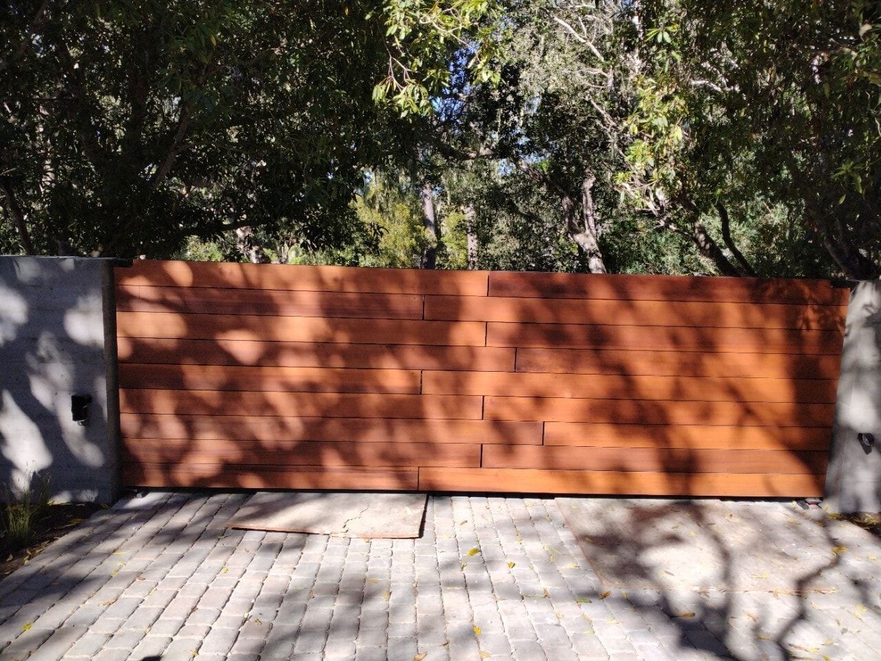 Orange brick wall behind a paved patio, with tree shadows across the scene.