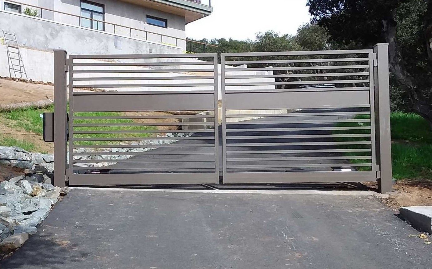 Metal driveway gate at the end of a sloped driveway beside a house and stone wall