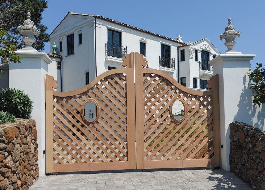 Wooden lattice gate before a white stucco villa with stone pillars and a blue sky