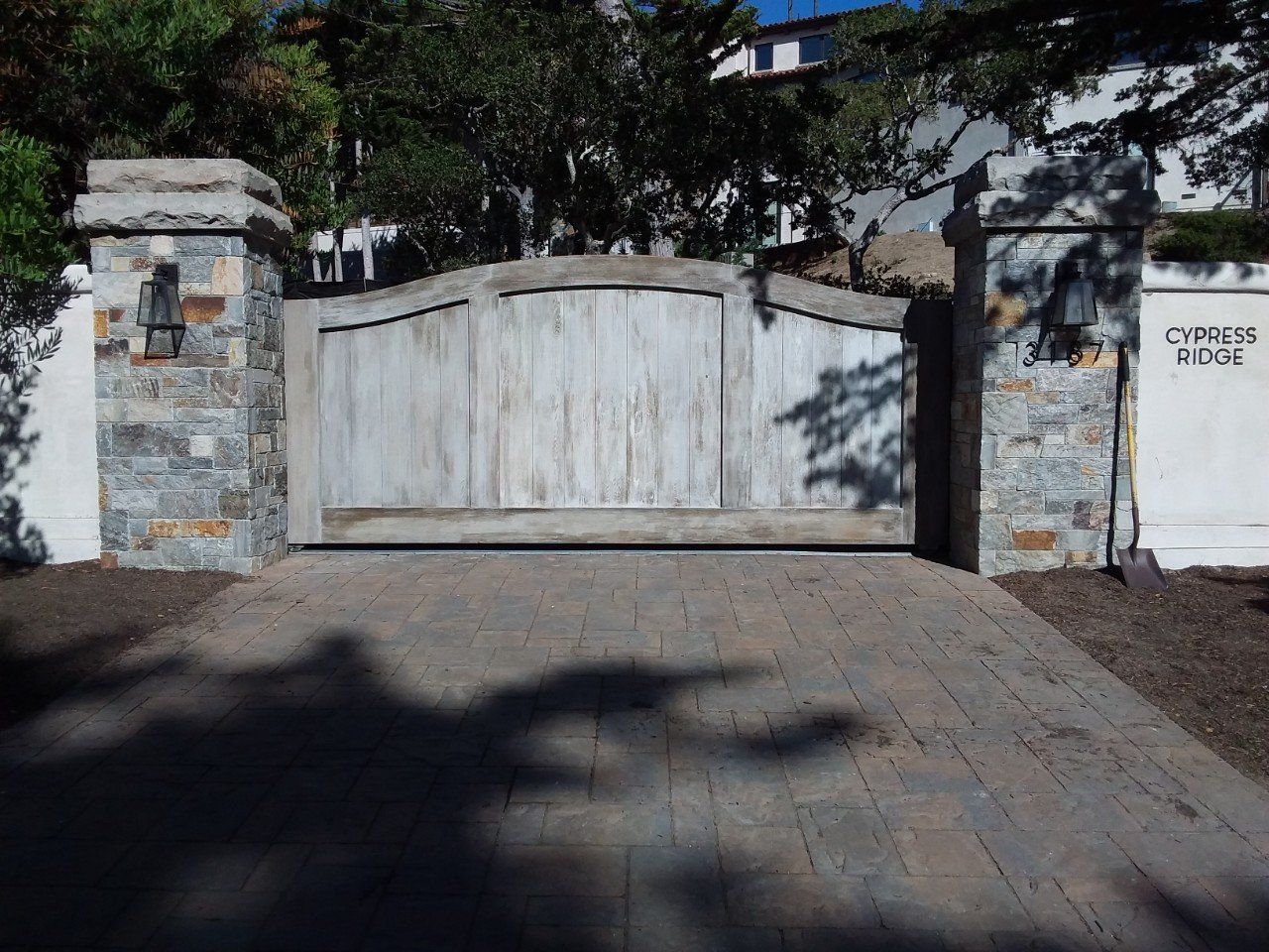 Wooden driveway gate between stone pillars with a sign reading “Queens Road”
