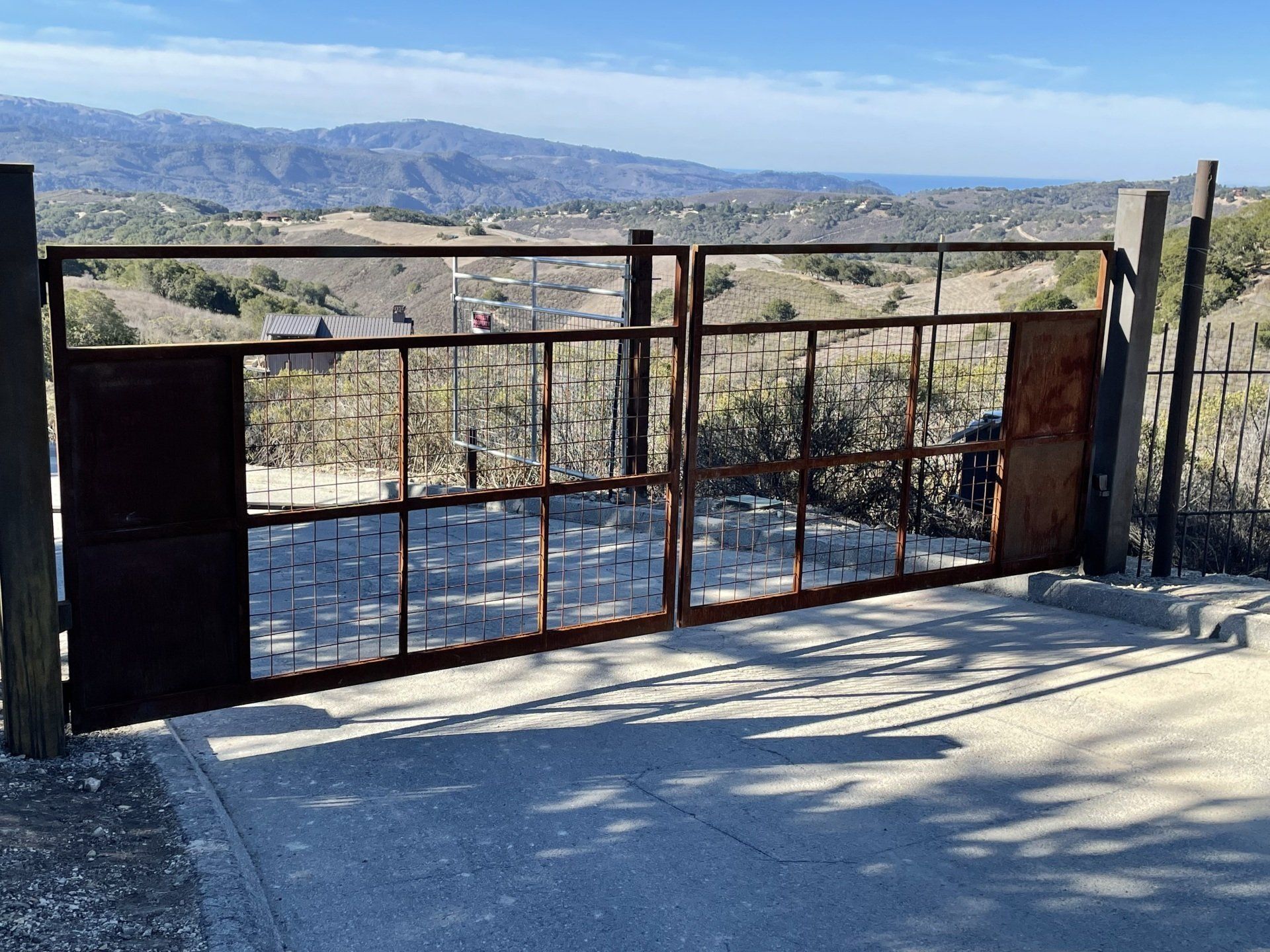 Rustic metal gate overlooking a sunlit valley with mountains in the distance