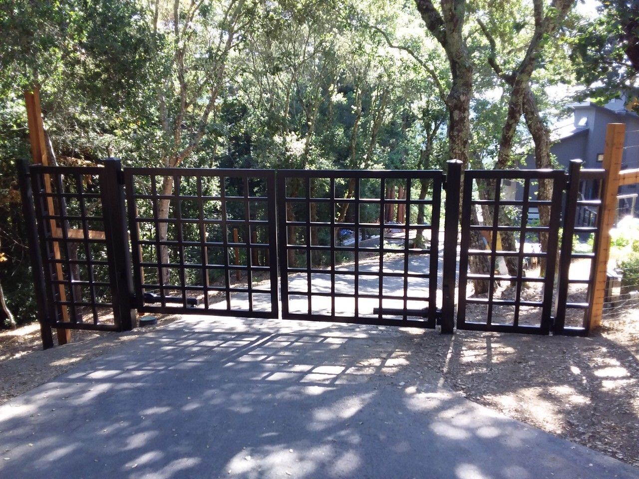 Black metal gate across a sunny wooded path, with trees and shadows behind it.