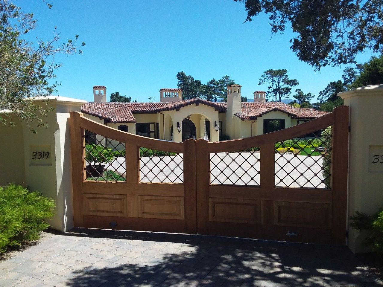 Closed wooden gate in front of a stucco house with red tile roof and trees under a clear blue sky