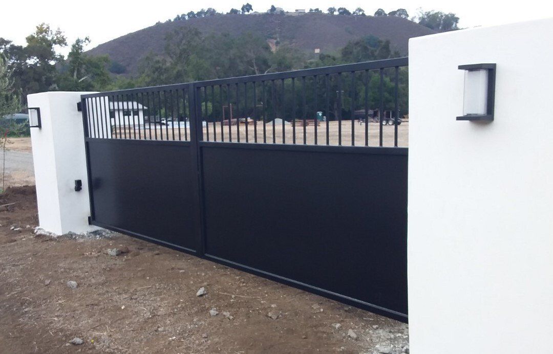 Black metal sliding gate between white walls with hillside in the background