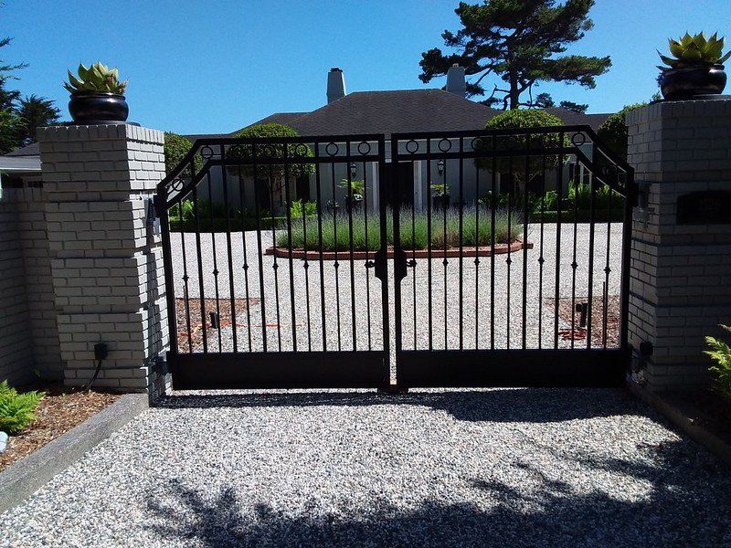 Black wrought-iron gate between stone pillars at the entrance to a gravel driveway