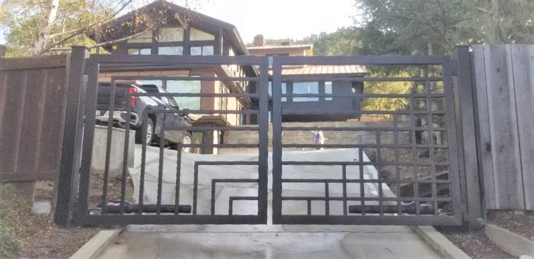 Closed metal gate at the entrance to a driveway with houses and a parked car beyond