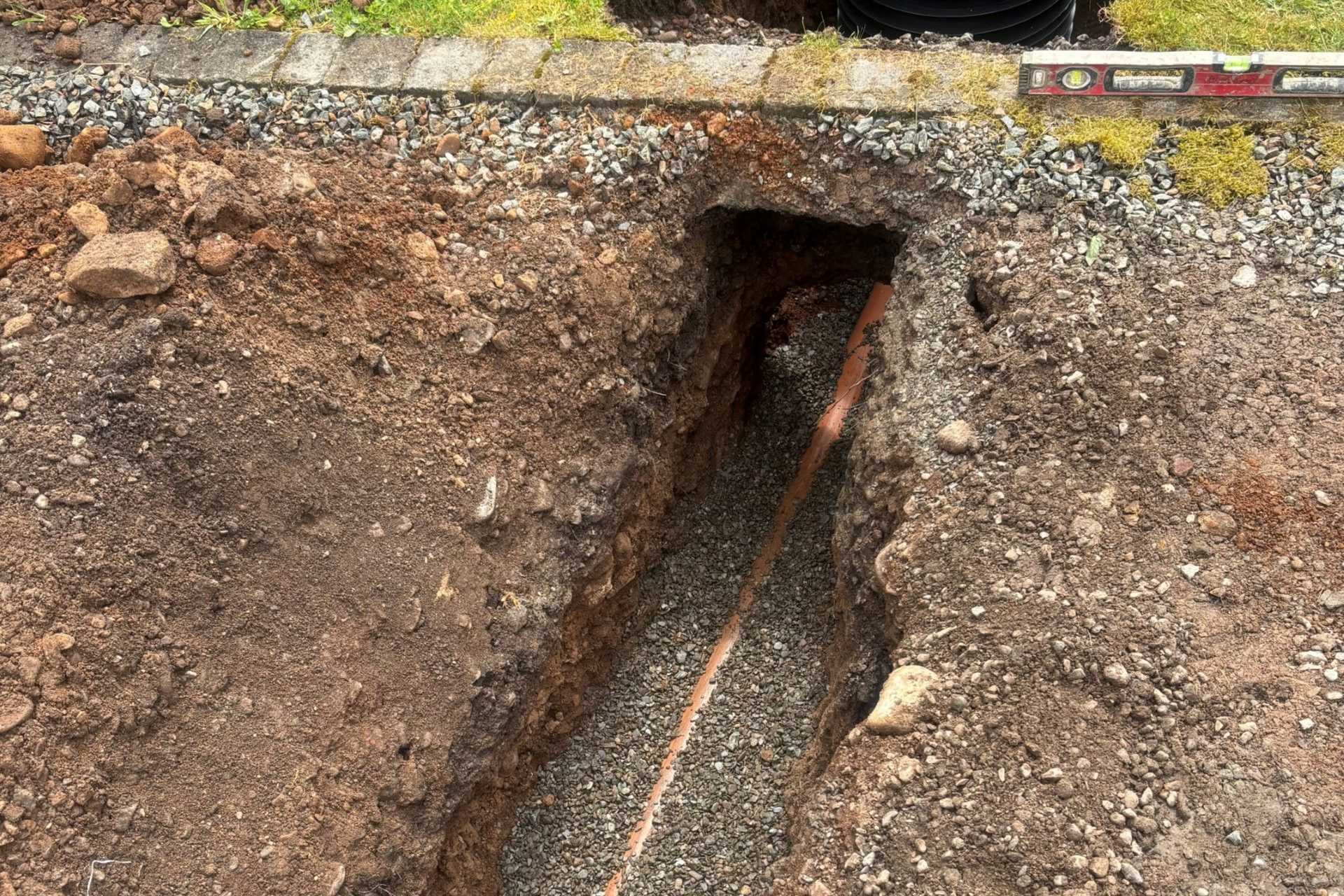 Cracked soil with a narrow trench or pipe opening near a concrete edge
