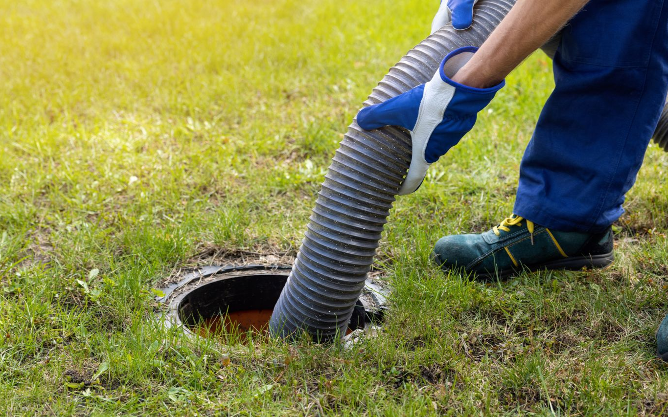 Worker cleaning a manhole with a vacuum hose on a grassy lawn