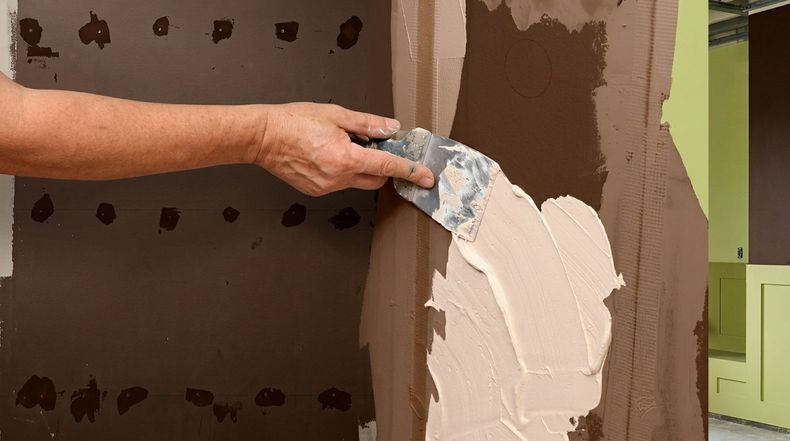 Hand spreading white plaster on a brown wall during interior repair
