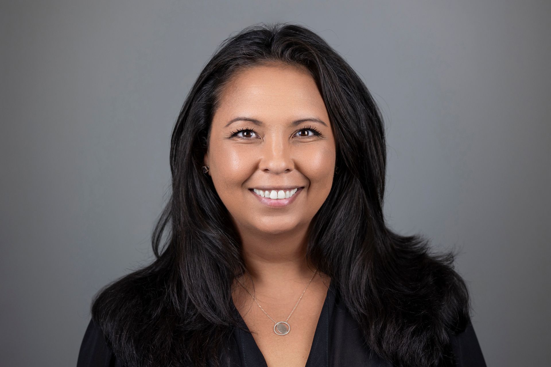 A woman wearing a black shirt and earrings is smiling for the camera.