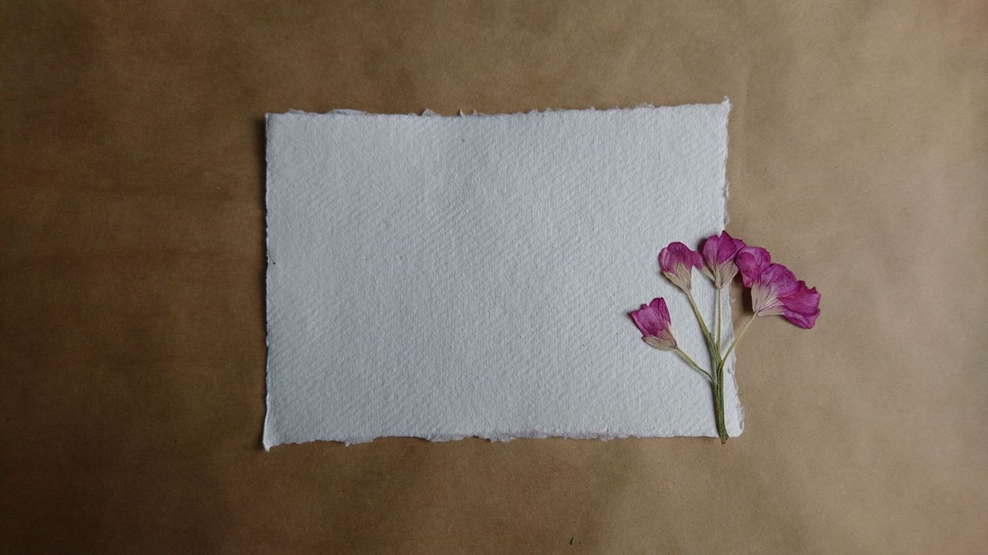 Wit, gestructureerd papier met gescheurde randen, een bruine achtergrond en kleine roze bloemen.