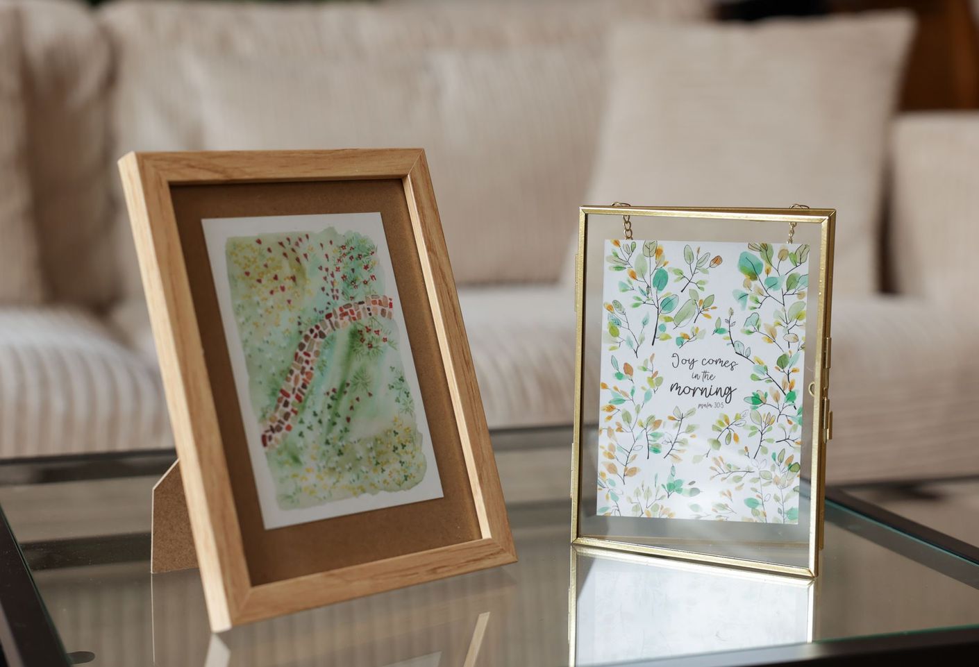 Twee ingelijste kaarten staan op een tafel. De kaarten bevatten bloemen en bladeren.