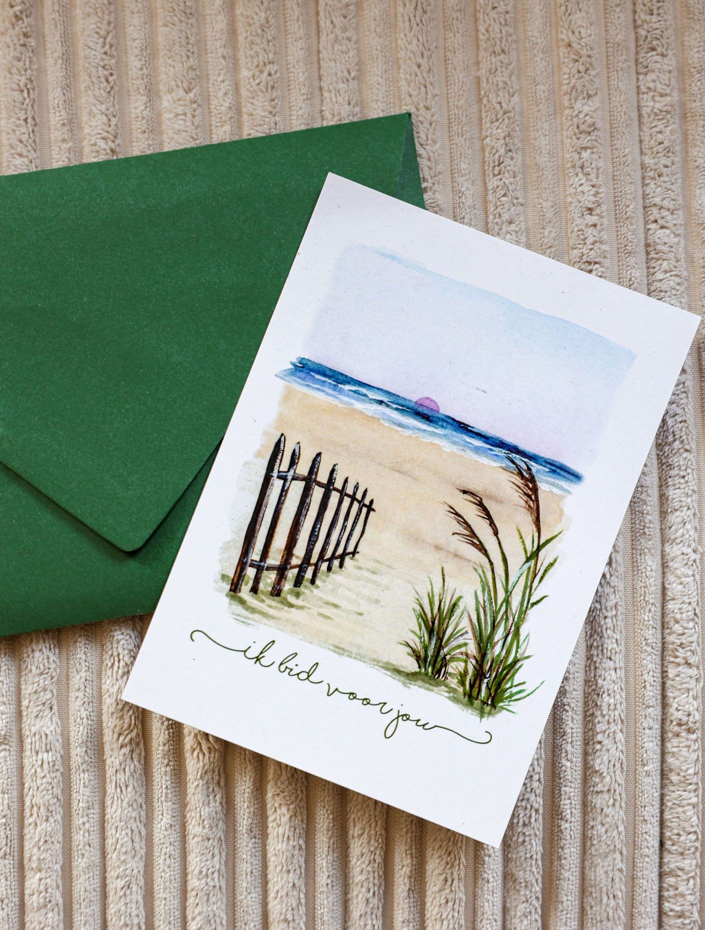Kaart met strandtafereel en groene envelop. Zandstrand, hek, blauw water, blauwe lucht en groen.